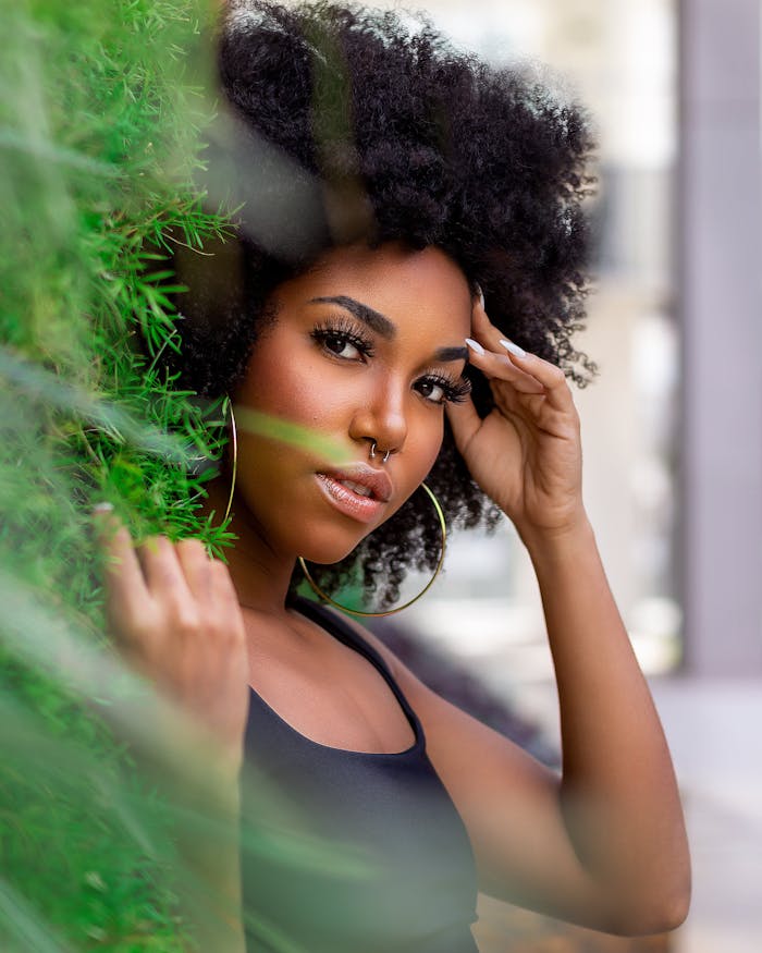 Elegant portrait of a woman with afro hair and hoop earrings, posing outdoors.