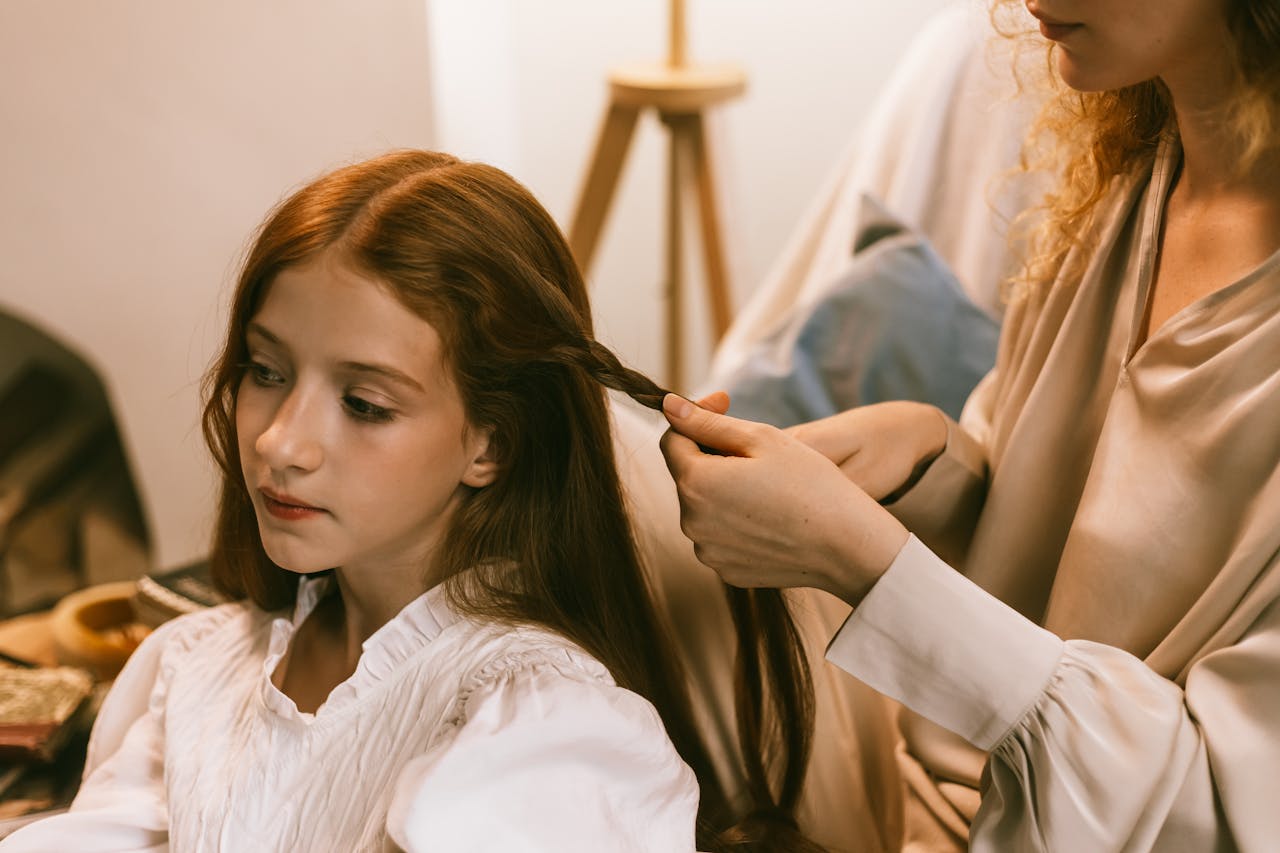 A woman braiding a young girls hair in a warm, cozy home setting.